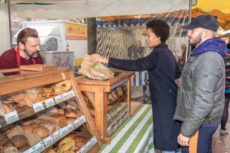 Eine Kundin kauft eine Tüte mit Backwaren auf dem Marktstand eines Bäckers.